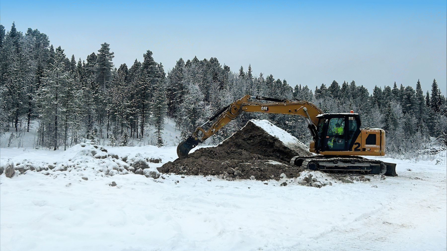 En elev kör en grävmaskin på övningsområdet i Kiruna i vacker vintermiljö