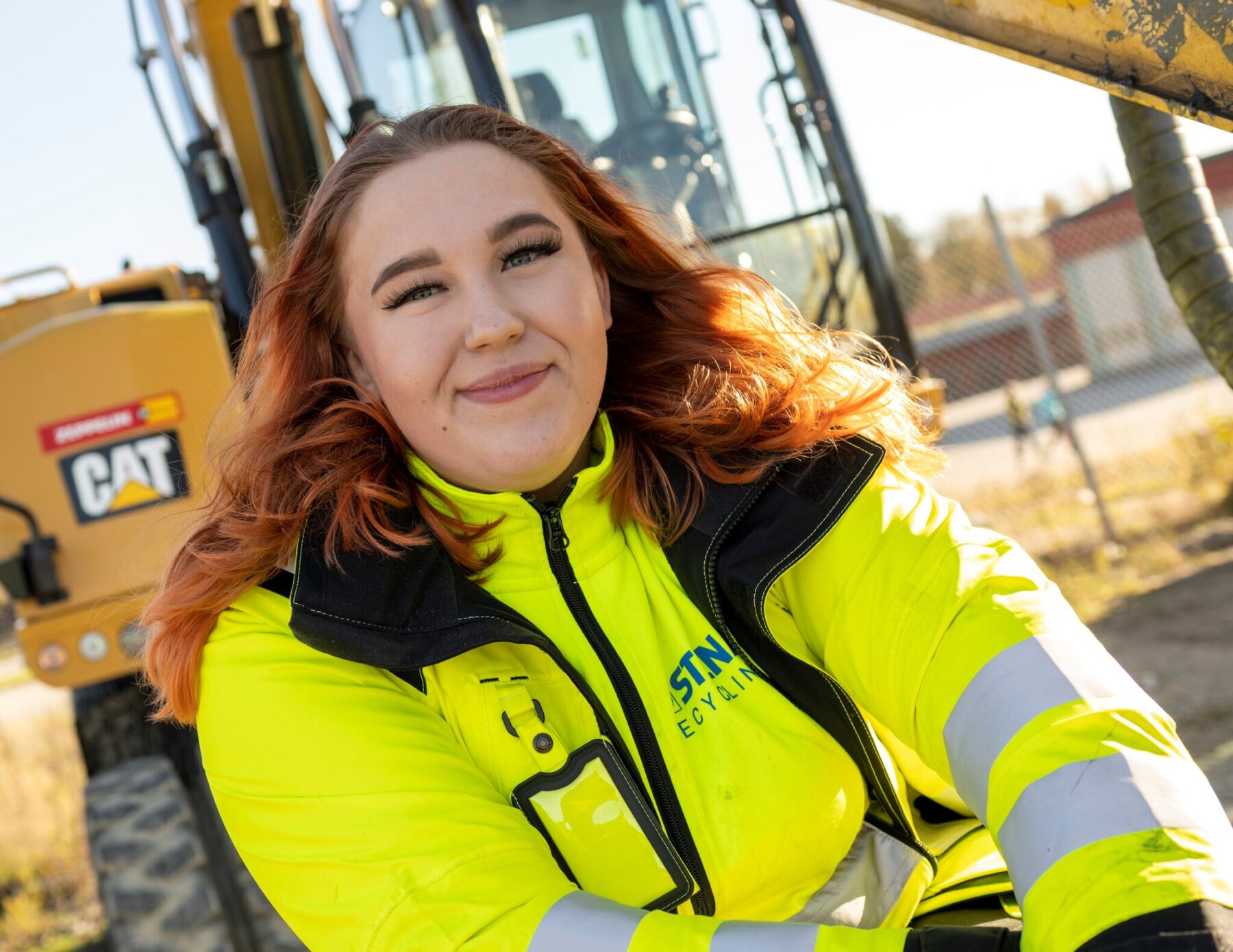 En kvinnlig maskinförare framför en gul grävmaskin